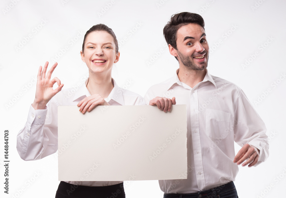 Young happy couple showing presentation pointing on placard over gray background Young happy couple showing presentation pointing on placard over gray background