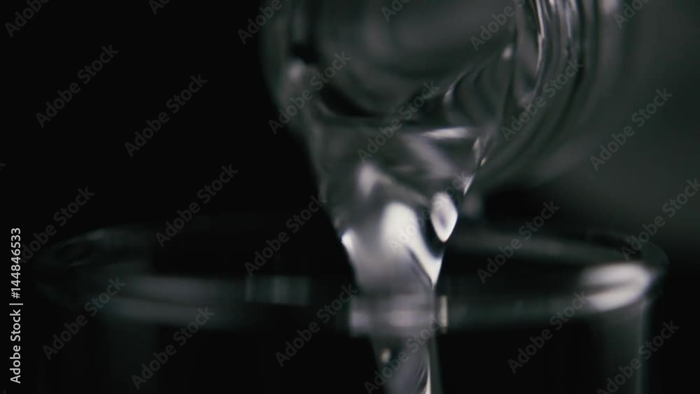 Vodka, water, clear liquid, drink pouring from the neck of a bottle, close-up, on a black background. Slow motion Vodka, water, clear liquid, drink pouring from the neck of a bottle, close-up, on a black background. Slow motion