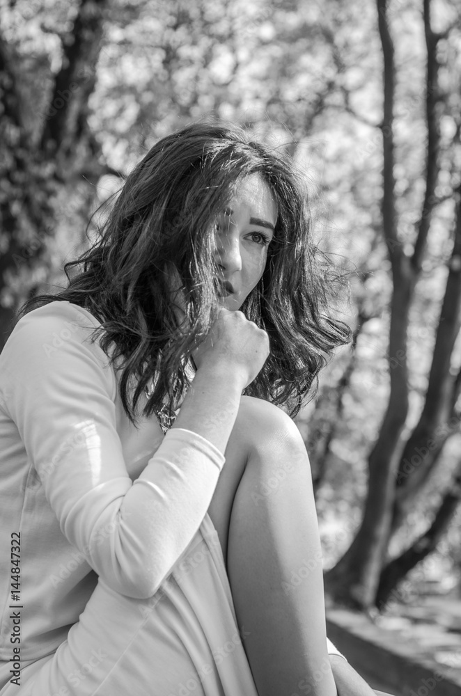 Young beautiful girl sits sad in a white dress in a street in the spring city of Lviv