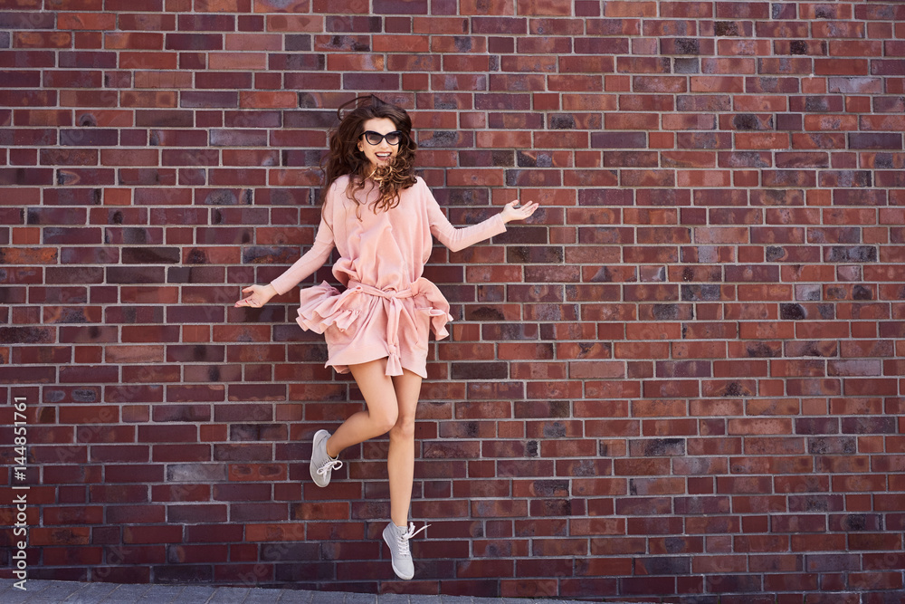 Joyful Young woman having fun jumping against brick wall Joyful Young woman having fun jumping against brick wall