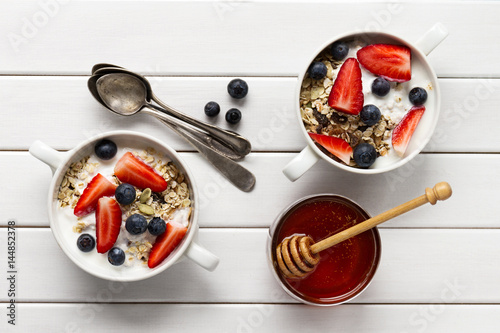 Tasty colorful Breakfast with Oatmeal, Yogurt, Strawberry, Blueberry, Honey and Milk on White Wooden Background with Copy Space. Top View.