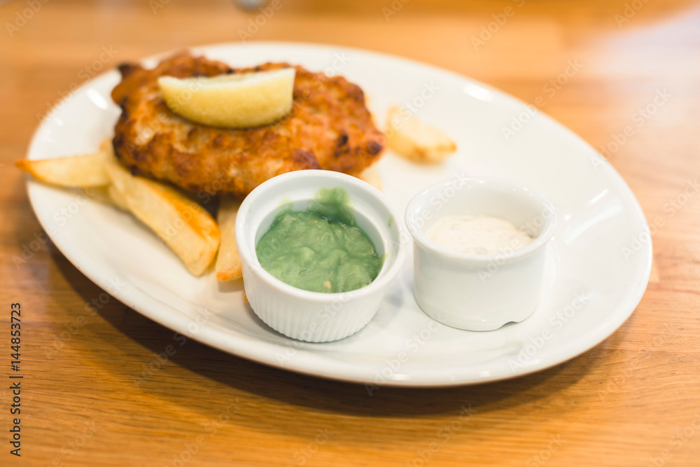 Mashed peas and sauce on plate with fish and chips.