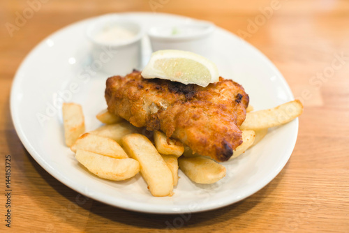 Fish and chips with lemon on white plate.