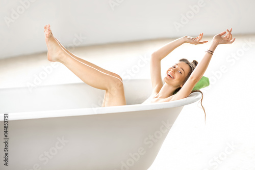 Beautiful excited woman relaxing lying in the bathtube in the white bathroom