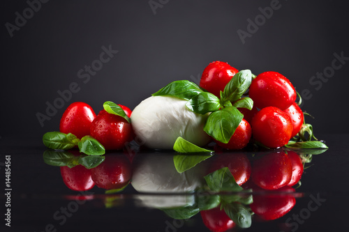 Mozzarella cheese with basil and tomatoes on black table