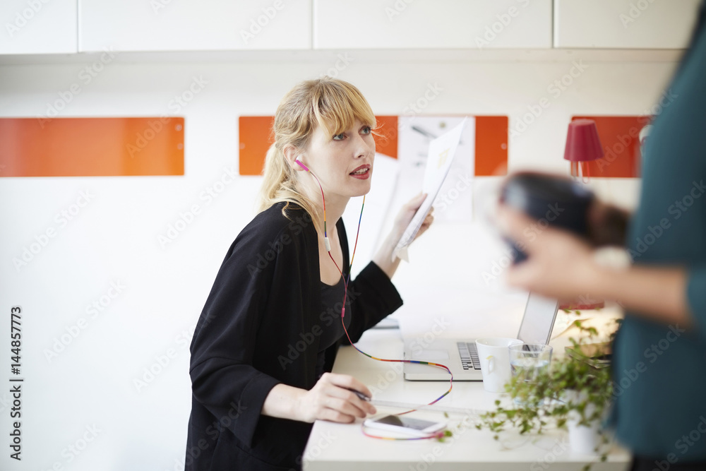 Mid adult businesswoman using hands-free device at table in office Mid adult businesswoman using hands-free device at table in office
