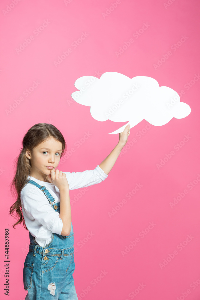 Adorable little girl in denim overalls holding blank speech bubble and thinking on pink Adorable little girl in denim overalls holding blank speech bubble and thinking on pink