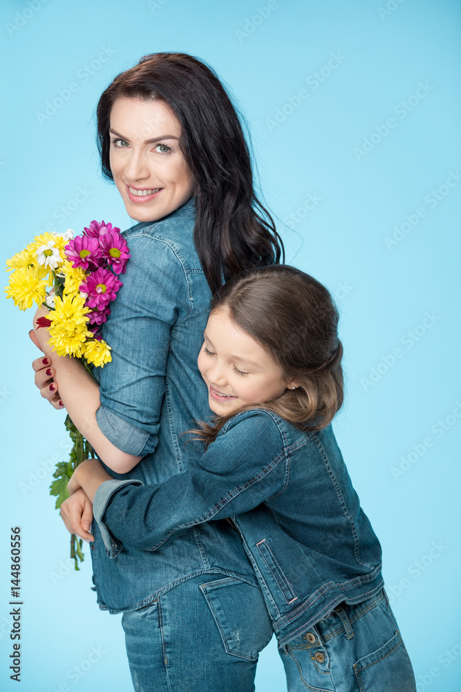 happy mother and daughter hugging and holding flowers in studio on blue, Happy mothers day happy mother and daughter hugging and holding flowers in studio on blue, Happy mothers day
