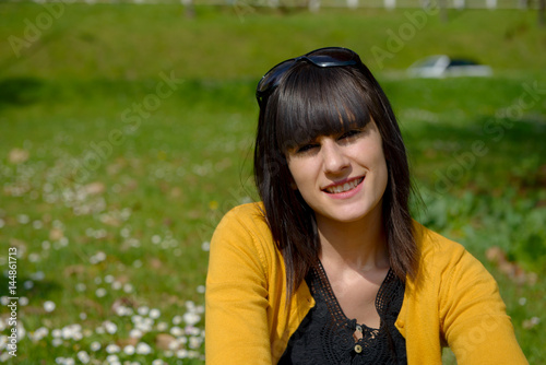 young brunette girl sitting on grass in park, outdoors
