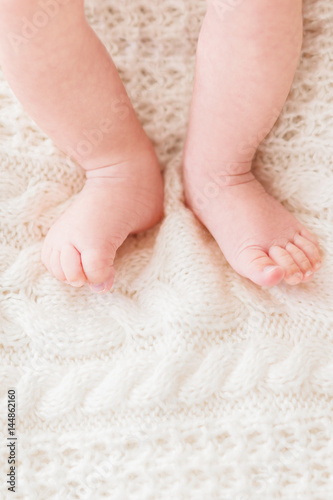 Baby's feet on white knitted background. Little child's bare feet. Cozy morning bedtime at home. Place for text.