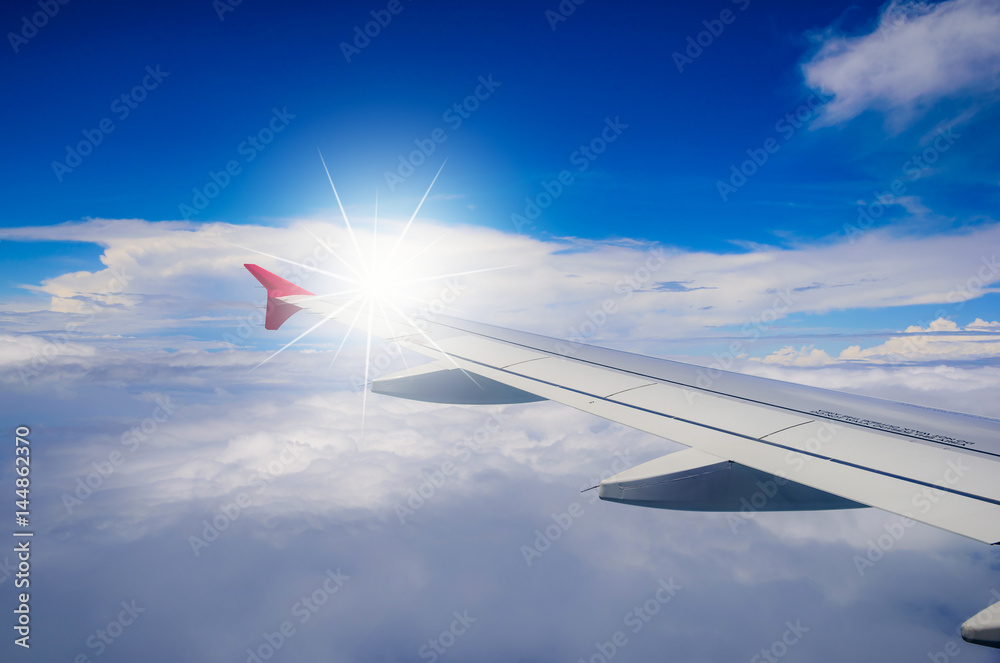 Fototapeta premium Wing of airplane flying above the clouds in the blue sky background.