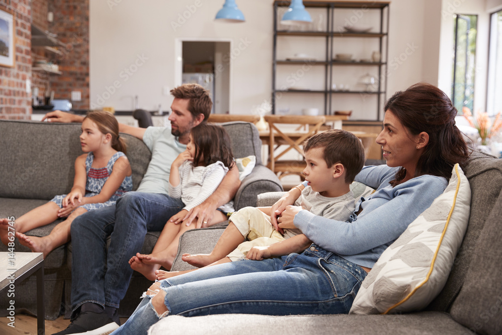 Family Sit On Sofa In Open Plan Lounge Watching Television Family Sit On Sofa In Open Plan Lounge Watching Television