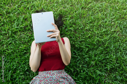 Fototapeta Naklejka Na Ścianę i Meble -  Woman lay down on green grass and using tablet