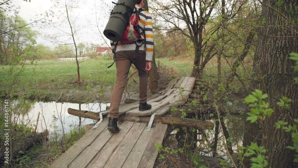Tourist with a backpack crosses a wooden bridge across the river. slow motion Tourist with a backpack crosses a wooden bridge across the river. slow motion
