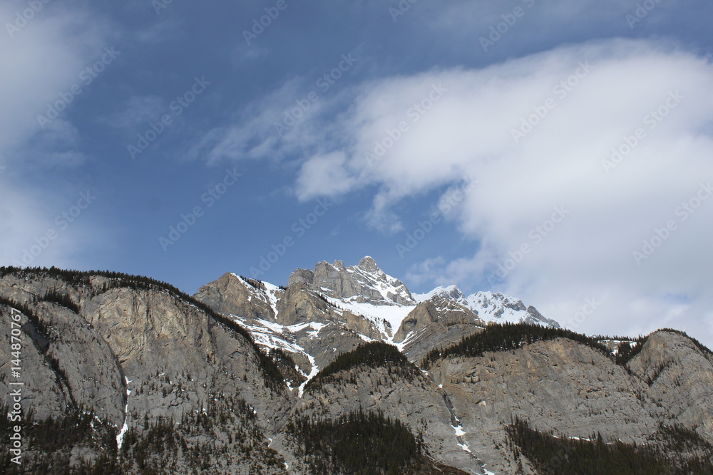 Rocky mountains and trees with blue sky and clouds closeup Rocky mountains and trees with blue sky and clouds closeup