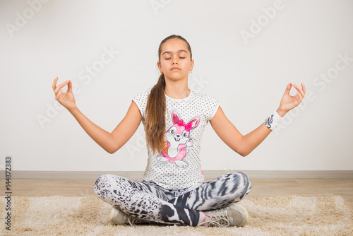 Girl teenager doing physical exercises after school. Girl doing exercises while sitting, like a lotus position. Girl in yoga pose. Meditation at home
