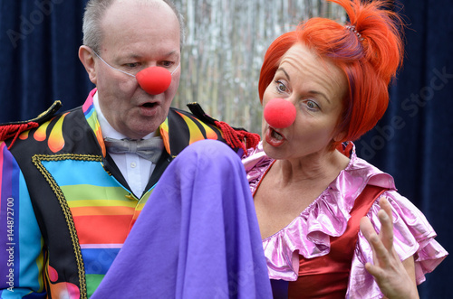 Two red nosed performers watch an elevating ball photo