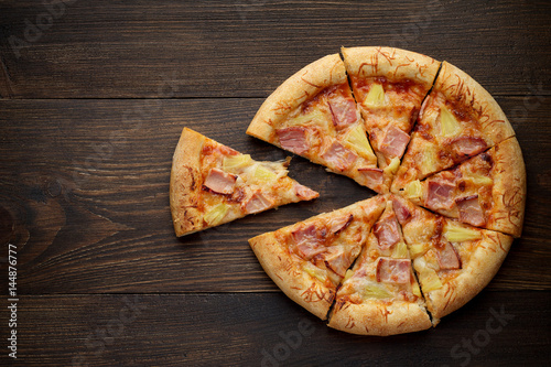Sliced hawaiian pizza with pineapple and ham on dark rustic wooden background.