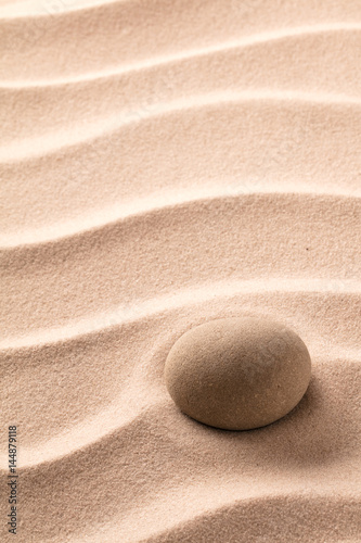 Round stone laying on rippled beach sand. Zen meditation minimalism. Concept for relaxation and concentration.
