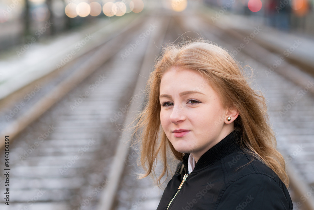 Young blonde girl posing. On background, out of focused railroad tracks