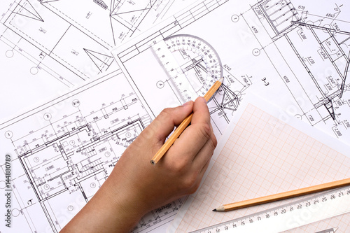 Man architect draws a plan , schedule , design , geometric shapes with a pencil and transparent protractor. On the desktop , on the graph paper is a transparent ruler and pencil