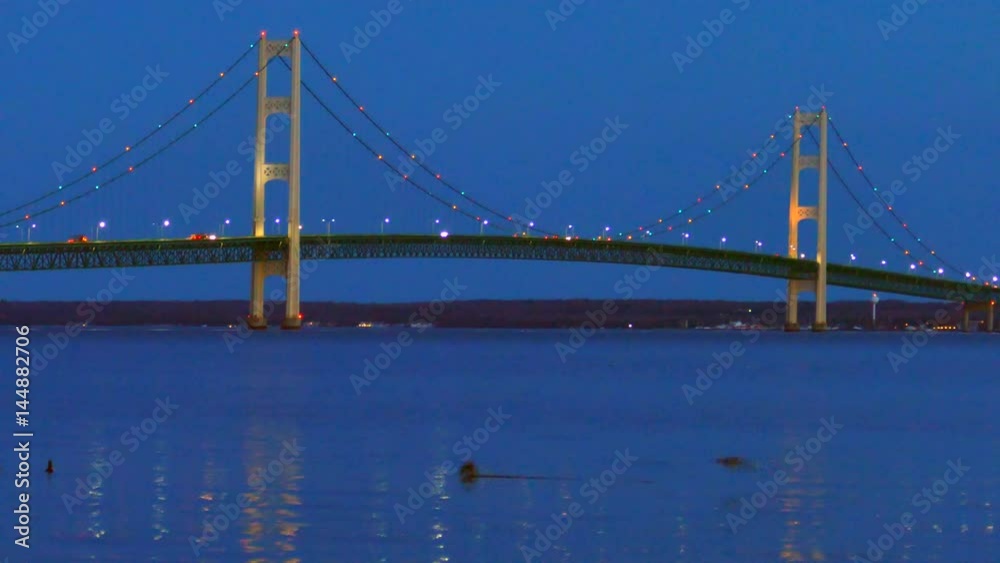 The lights of scenic, Majestic Mackinac Bridge sparkle in deep blue predawn twilight as ducks playfully swim in the foreground, Upper Peninsula of Michigan. The lights of scenic, Majestic Mackinac Bridge sparkle in deep blue predawn twilight as ducks playfully swim in the foreground, Upper Peninsula of Michigan.