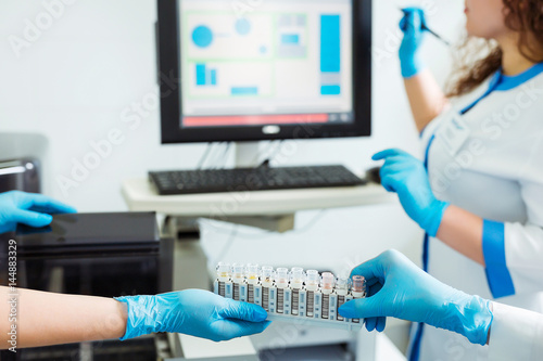 Biochemical analysis of blood. Hands of laboratory assistant loading sample tubes before loading to biochemical analyzer and inputing data to computer