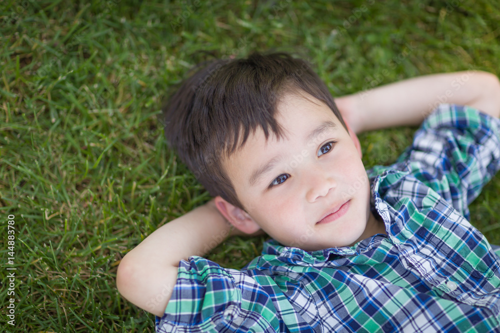 Thoughtful Mixed Race Chinese and Caucasian Young Boy Relaxing On His Back Outside On The Grass Thoughtful Mixed Race Chinese and Caucasian Young Boy Relaxing On His Back Outside On The Grass
