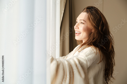 Cheerful woman in bathrobe smiling and looking at the window