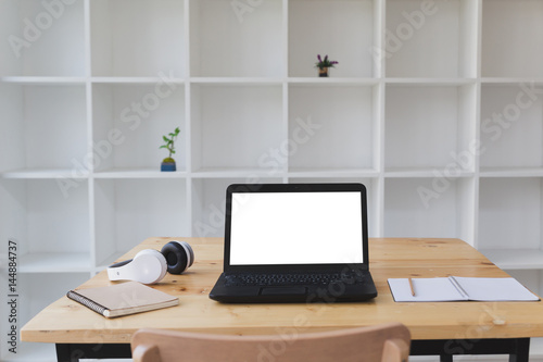 Desk table with laptop, headphone, notepad with white bookshelf background