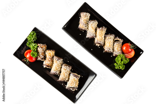 Eggplant rolls with cheese, garlic and sesame on black plates with herbs and tomato. Top view and isolated on white