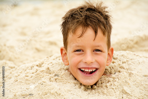 Foto little boy buried in the sand on beach