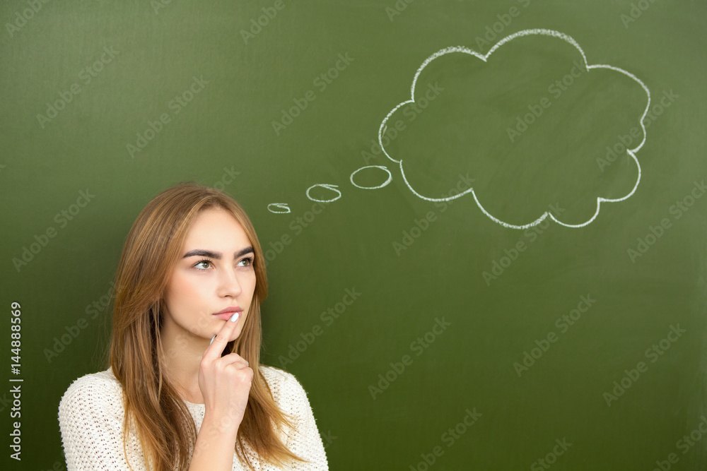 Young woman thinking with a blank thought bubble drawn on a chalkboard behind her