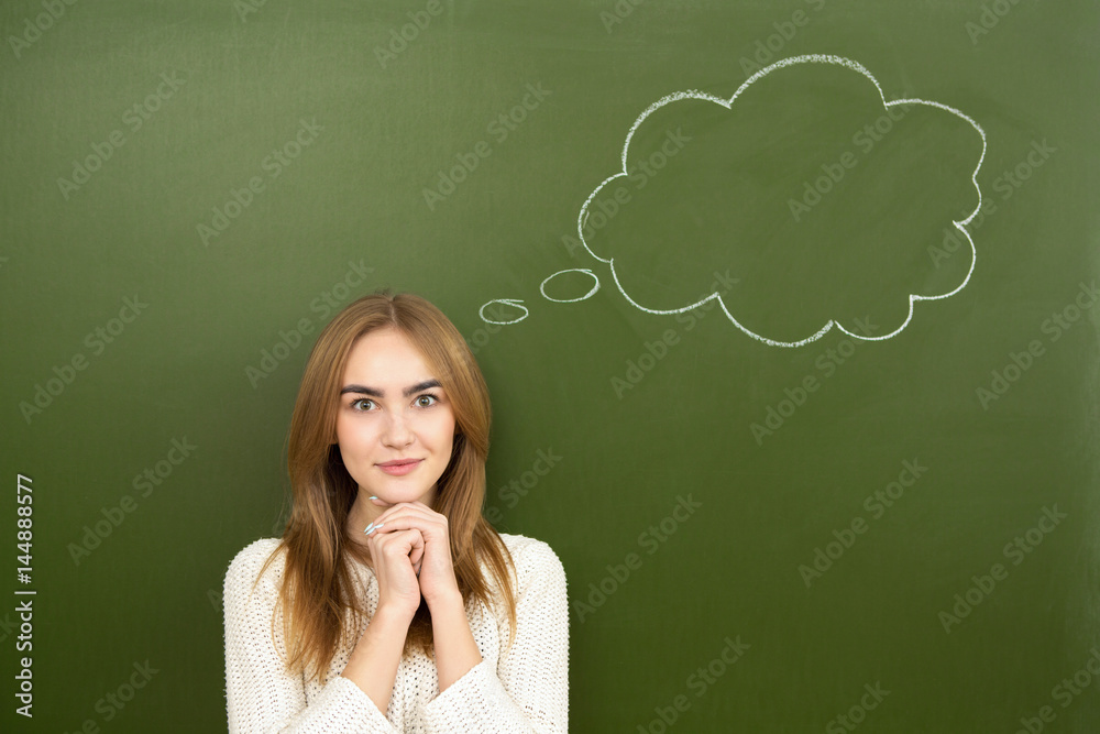 Beautiful young woman posing near idea thought bubble drawn behind her on a green chalkboard Beautiful young woman posing near idea thought bubble drawn behind her on a green chalkboard