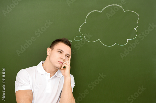 Young man thinking with a blank thought bubble drawn on a chalkboard behind him