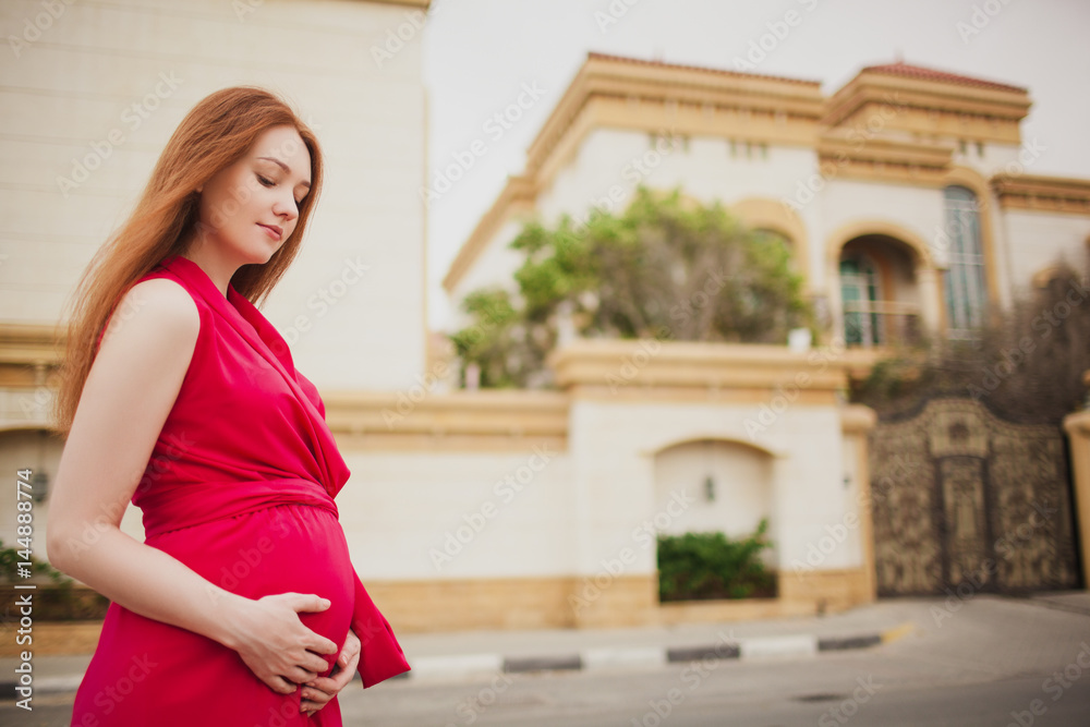 Cute red-haired pregnant girl in a red dress. On the background of the Villa.