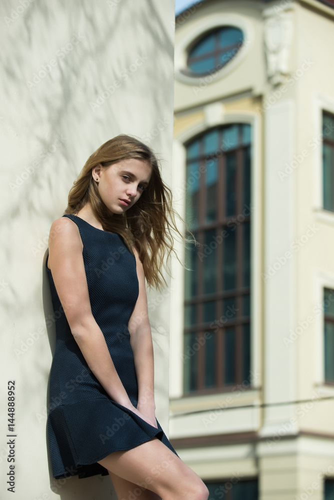 Pretty girl in fashionable black dress at building wall