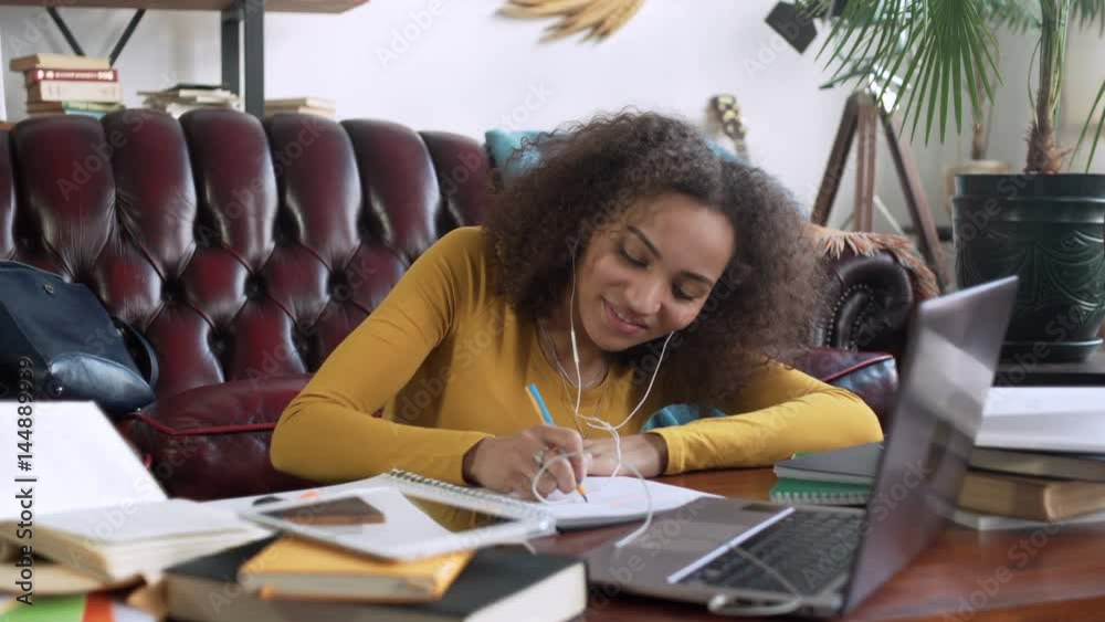 young african woman take part in video call using app on laptop computer for education online and remote working discussion making notes in notebook sitting on floor near sofa at home during sunny day