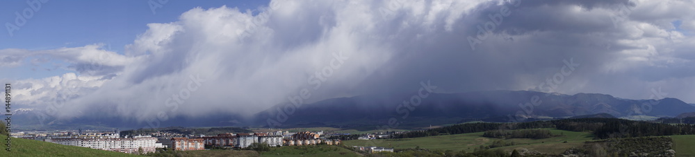 Panorama of rains in distance over mountain and city from meadow on a cloudy day. Slovakia