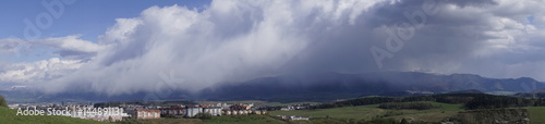 Panorama of rains in distance over mountain and city from meadow on a cloudy day. Slovakia