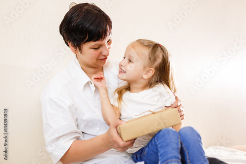 Beautiful brunette woman showing a book to her baby while sitting on a bed in her apartment