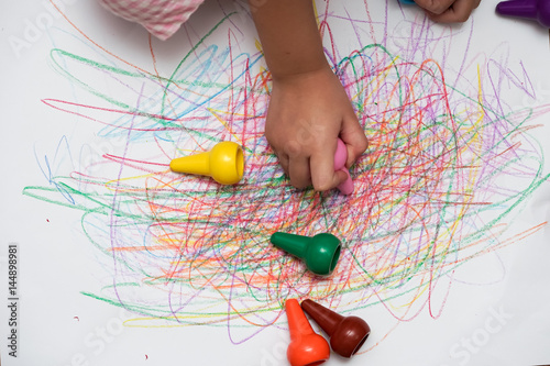 A hand of baby drawing lines and shapes with colorful crayons. The crayons can put in the fingers to draw easily.