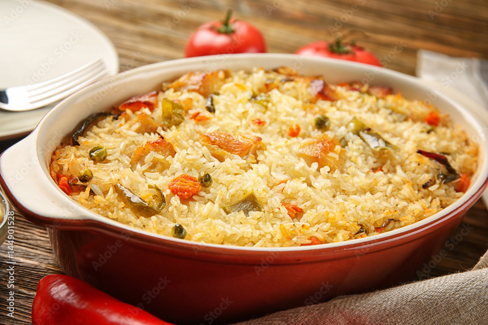 Tasty rice with chicken and vegetables in baking dish on kitchen table Tasty rice with chicken and vegetables in baking dish on kitchen table