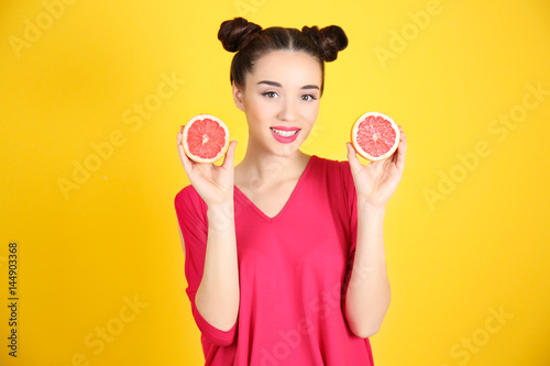 Beautiful young woman with grapefruit halves on yellow background