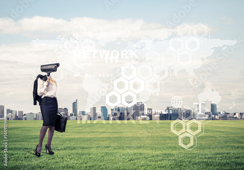 Camera headed woman standing on green grass against modern citys
