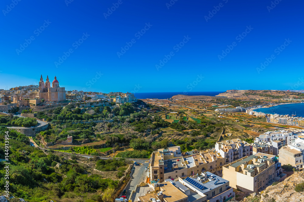 Il-Mellieha, Malta - Beautiful panoramic skyline view of Mellieha beach and Mellieha town on bright summer day with Paris Church, Agatha Red Tower and island of Gozo at background with clear blue sky