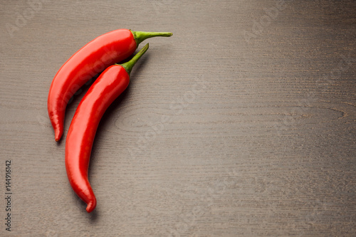 two fresh raw red hot chilli pepper on a wooden background tied with a rope