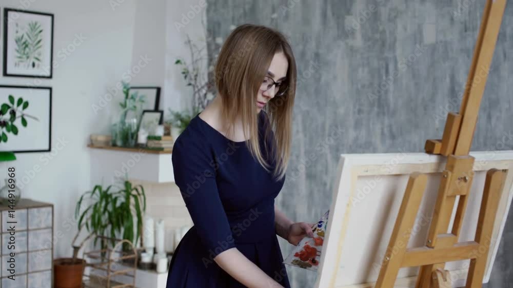Beautiful handsome girl in dress is adding collor on her pallette to continue painting Beautiful handsome girl in dress is adding collor on her pallette to continue painting