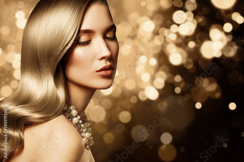 Fashion portrait of young caucasian model with gold jewelry on golden background. Beautiful blonde woman with long shiny hair. Glamour trendy accessories and hairstyle.
