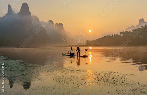 Cormorant fisherman throws a net with ancient traditional chinese bamboo boats at sunrise - Xingping, China photo
